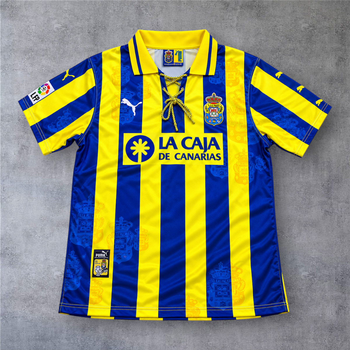 Camisola de futebol A minha loja Las Palmas 1998/99, listada em azul e amarelo com gola de cordões e logótipo Puma.