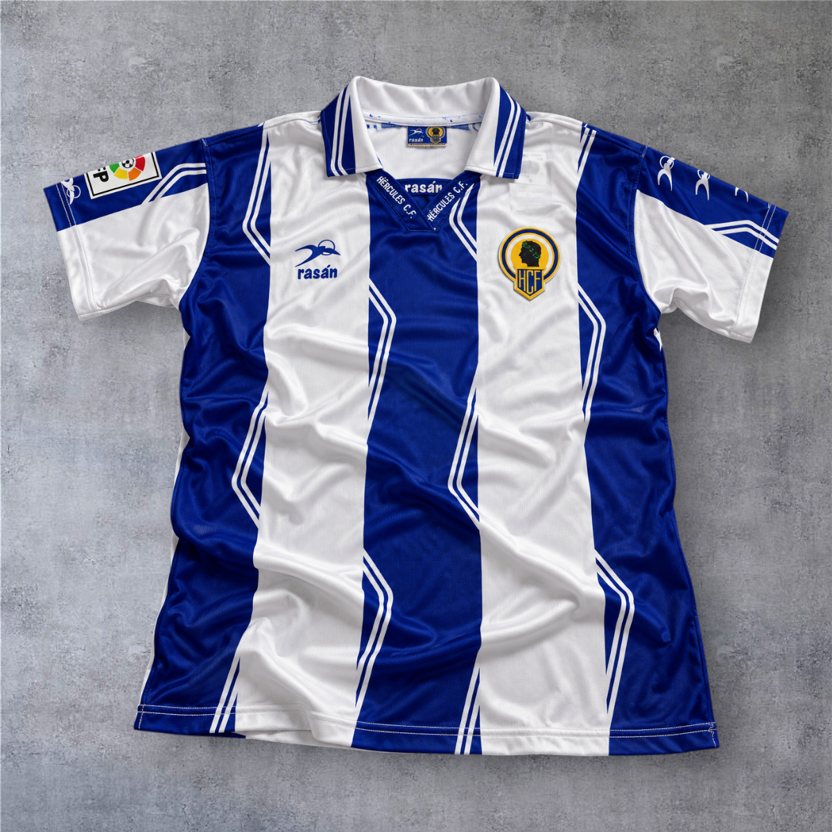 Camisola de futebol A minha loja do Hercules CF 1997/98, listada em azul e branco com gola polo e emblema do clube.