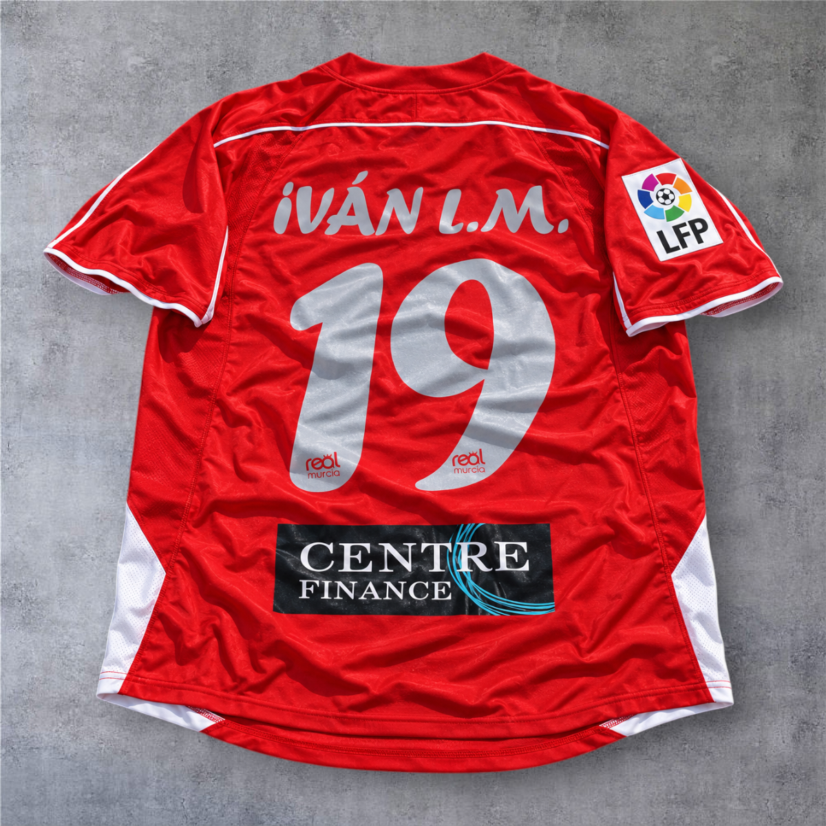Camisola de futebol A minha loja do Real Murcia 2006/07, vermelha, com nome Ivan L.M. e número 19 nas costas.