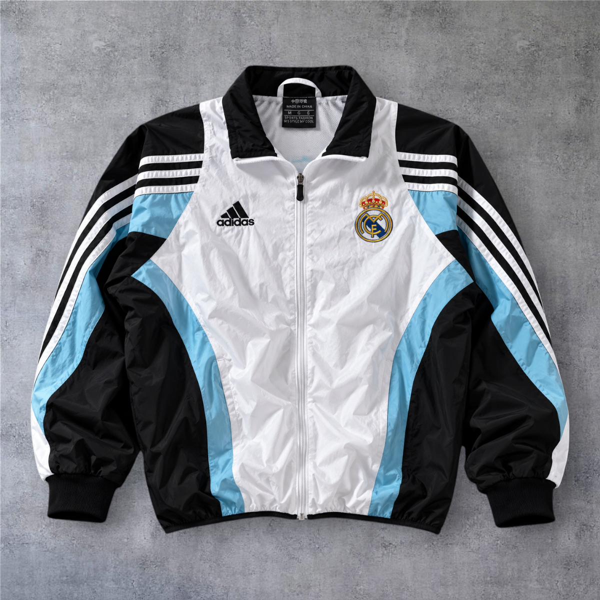 Casaco vintage Real Madrid 2003/04 da A minha loja, com fecho frontal, detalhes em branco, preto e azul claro.