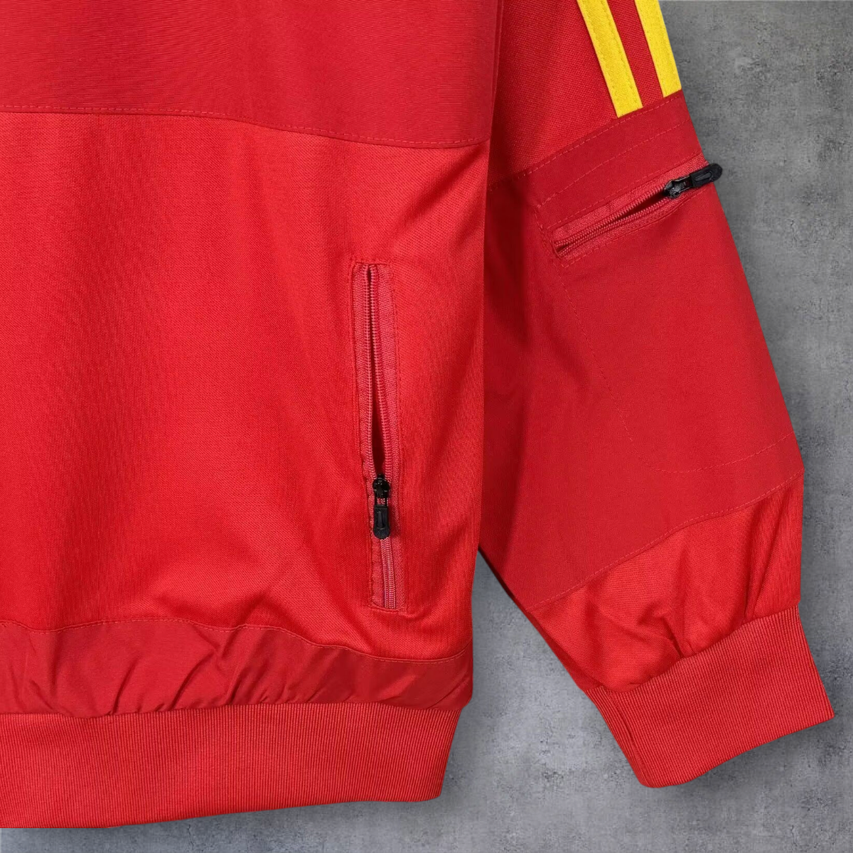 Detalhe da manga e bolso de fecho de correr do casaco vintage de Espanha 2010 da A minha loja em vermelho e amarelo