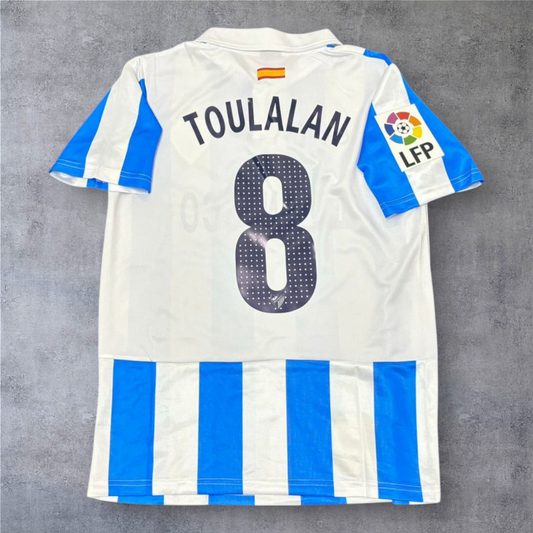 Camisola de futebol A minha loja Málaga 2012-13, branca e azul, com nome Toulalan e número 8 nas costas.