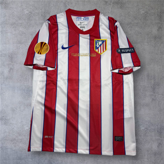 Camisola oficial A minha loja do Atlético Madrid 2011/12, listada a vermelho e branco com detalhes da final da Liga Europa.