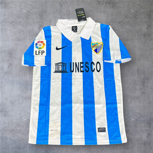 Camisola de futebol A minha loja Málaga 2012-13, listada em azul e branco com gola polo e patrocinador UNESCO.