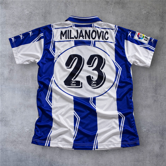 Camisola de futebol A minha loja Hercules 1997/98, listada em azul e branco com o nome Miljanovic e número 23 atrás.