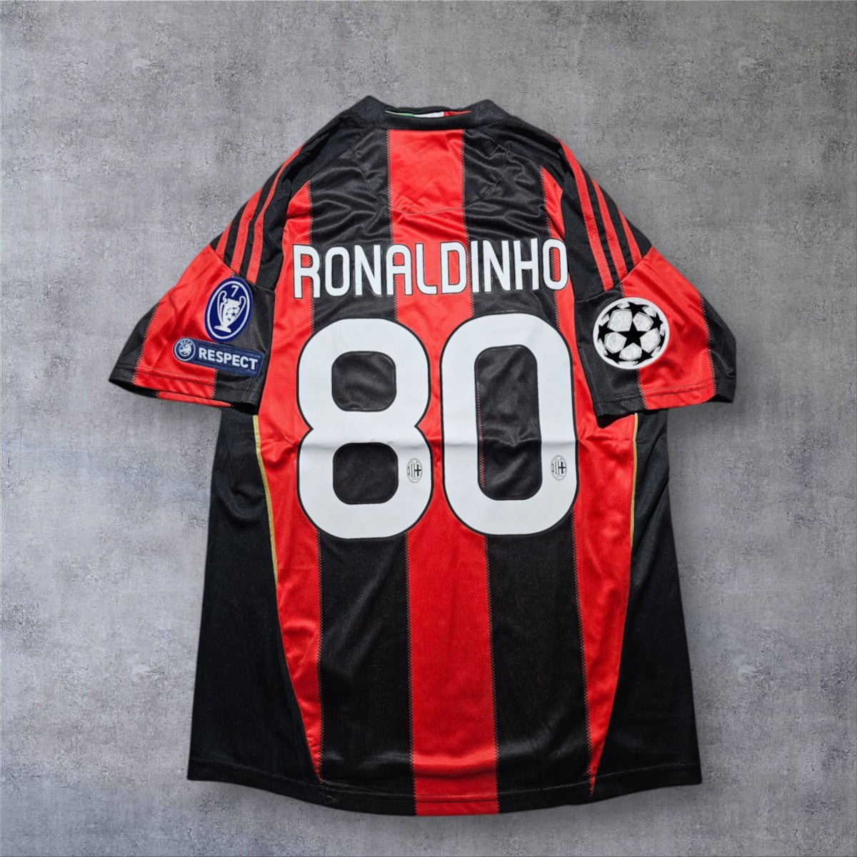 Camisola A minha loja do AC Milan 2010/2011 de Ronaldinho 80, com riscas pretas e vermelhas e emblemas Champions League